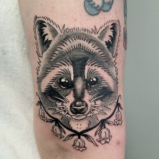Black and gray raccoon portrait framed by small flowers tattoo by Erin at Acme Tattoo Co.