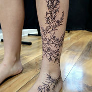 Black and gray botanical wraparound tattoo extending from the leg to the foot by Erin at Acme Tattoo Co.