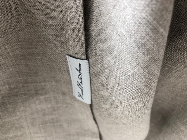 Close up of textured stonewashed European linen tablecloth in natural flax linen with Rural Route Seven logo brand label with light grey background and black font print
