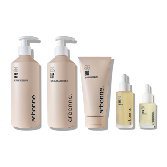 Five beige hair care products by Arbonne on a white background, including shampoo, conditioner, mask, serum, and oil.