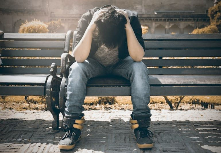 A worried man is sitting on a bench.