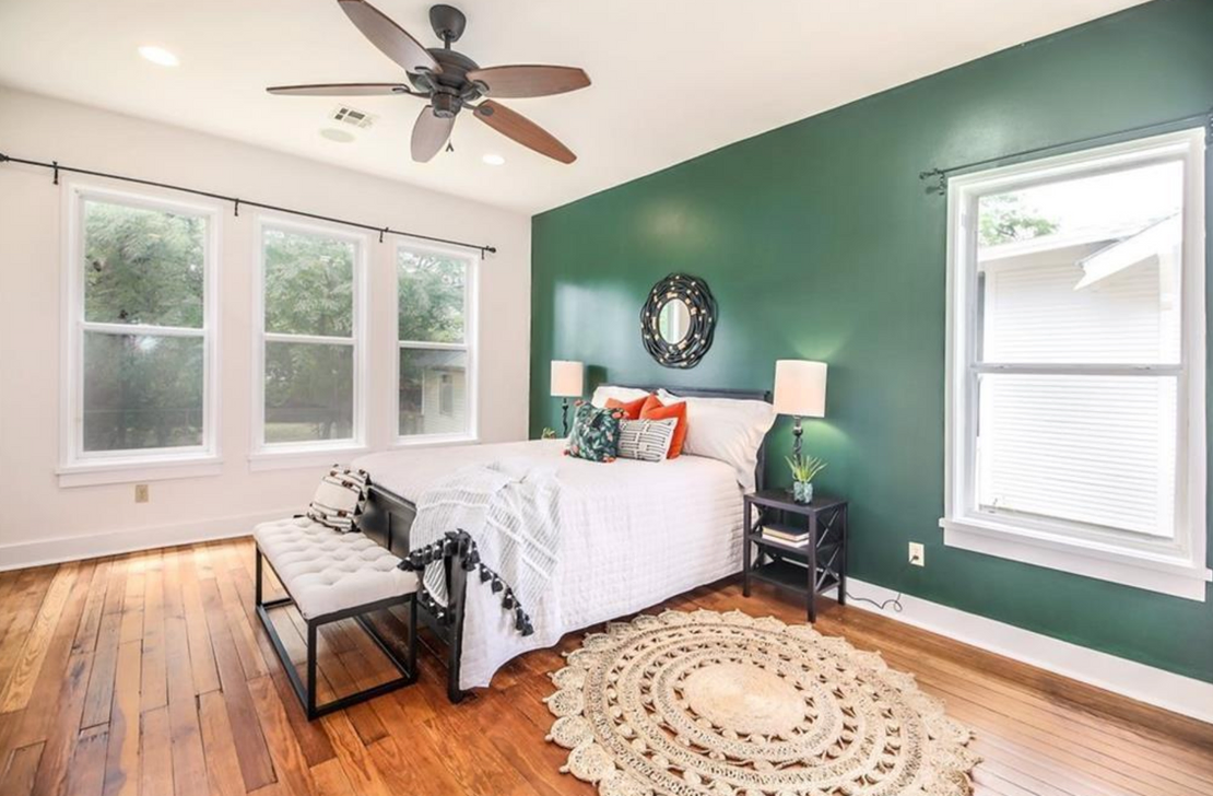 Bright and sunny bedroom with deep green statement wall, white bedding, and a round boho rug.