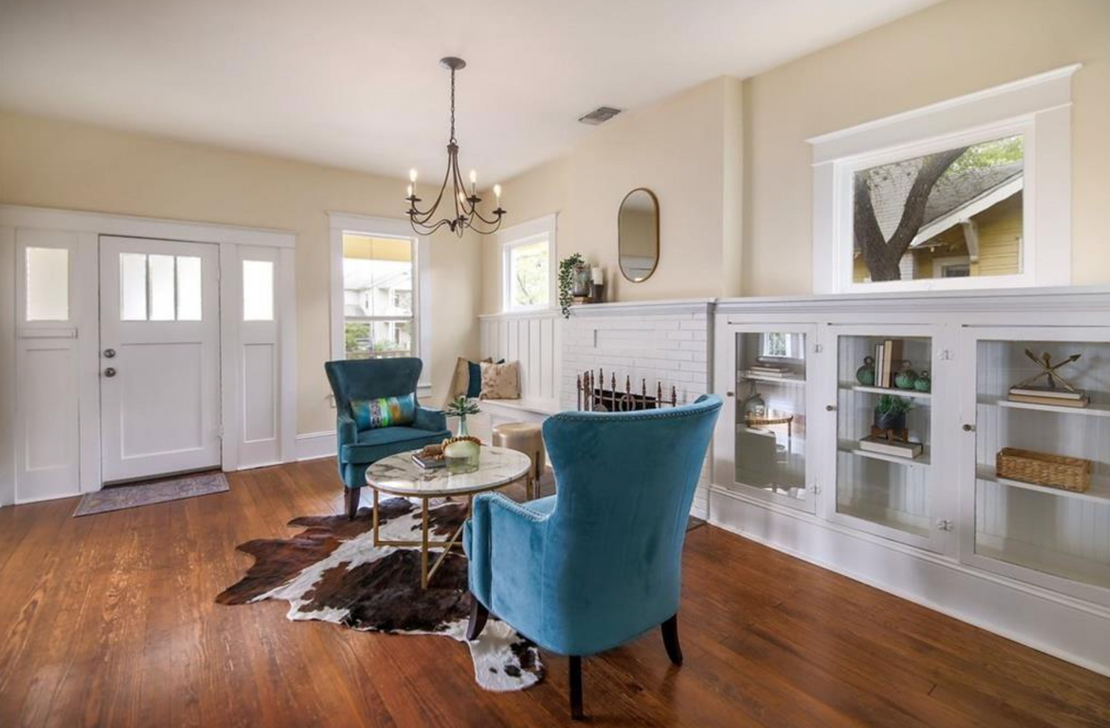 A charming home's front sitting room. Blue statement chairs at a faux marble table, with a brown and white cow skin rug in front of bright white built in cabinets and a fireplace