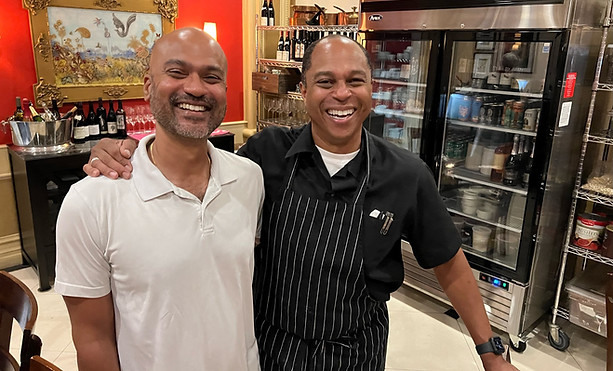 Edsel is next to his long term client. They are both smiling next to each other in his clients place of business.