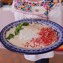 Cocinera tradicional agregando granada roja sobre la salsa de nuez de un auténtico Chile en Nogada en Puebla.
