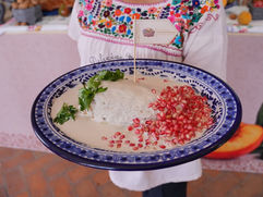 Cocinera tradicional agregando granada roja sobre la salsa de nuez de un auténtico Chile en Nogada en Puebla.