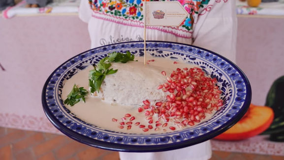 Cocinera tradicional agregando granada roja sobre la salsa de nuez de un auténtico Chile en Nogada en Puebla.