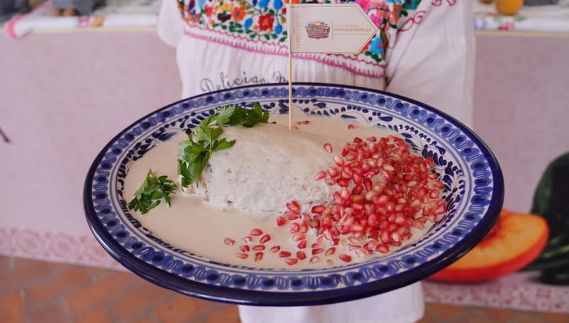 Cocinera tradicional agregando granada roja sobre la salsa de nuez de un auténtico Chile en Nogada en Puebla.