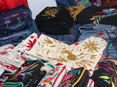 Manos de personas artesanas hidalguenses bordando una colorida pieza textil tradicional.