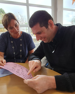 There is an image of a man and a woman looking at a piece of paper. the woman is supporting the man to read the information.
