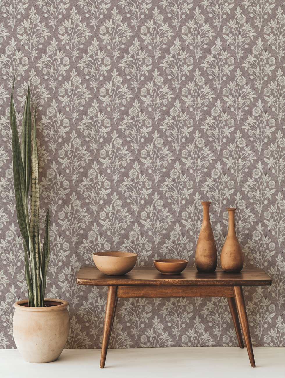A stylish interior with a hand-printed floral geometric wallpaper in soft mauve. The setting includes a mid-century modern wooden table adorned with handcrafted ceramic bowls and vases, complemented by a potted snake plant, creating a warm and organic atmosphere.