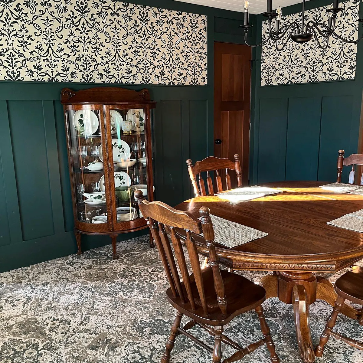 Dining room with dark green wood panelling and custom-matched wallpaper in a vintage damask pattern.