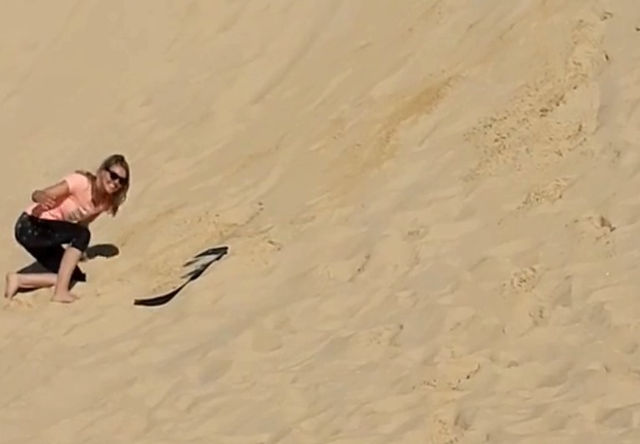 Frau rutscht mit einem Sandboard die Sanddünen in Anna Bay hinunter