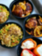 Meal prep containers featuring yellow rice with chicken and stuffed bell peppers by Kusi House.