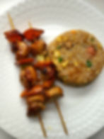 Grilled chicken skewers with colorful bell peppers served alongside a side of seasoned fried rice by Kusi House.