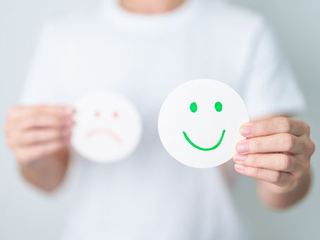 A person holding a smiley face and a sad face in the background