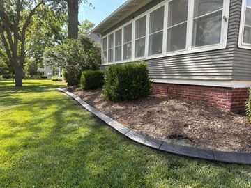 Curved decorative concrete curbing along house foundation with brick base and mature plantings
