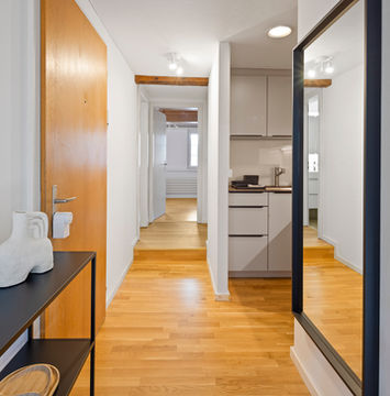 Interior hallway with wooden floor, white walls, and access to multiple rooms in Zug apartment.
