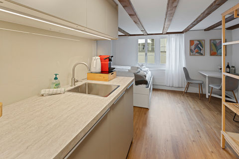 Open-plan kitchen and living area with coffee machine, compact counter, and bright space in Zug serviced apartment.
