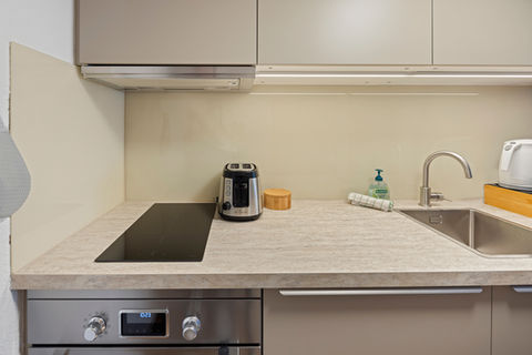 Compact kitchen with stovetop, coffee machine, sink, and storage in serviced apartment Zug Old Town.
