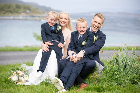 Brudepar sammen med barn som sitter i fanget mens de smiler og ser i kamera.