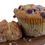 Thumbnail: Close up of a muffin with cranberries, cut in half, on wood surface.