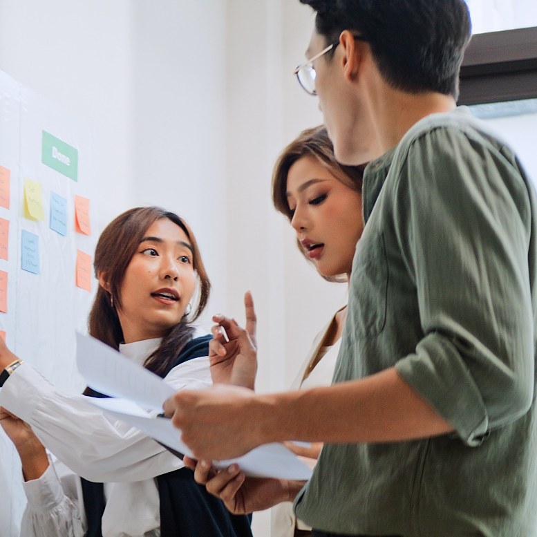 Three colleagues planning their work together at a wall of sticky notes