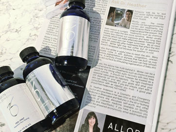 Blue ZO Skin Health skincare bottles on a newspaper article titled Ask Dr. Heather, resting on a marble tabletop.