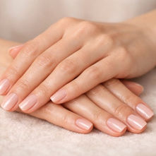Hands with neatly manicured nails rest on a soft, beige surface. The nails are painted a pale pink, conveying a calm and elegant mood.