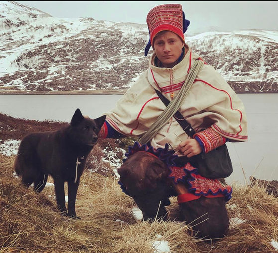 Sámi reindeer herder with dog and reindeer in traditional winter clothing