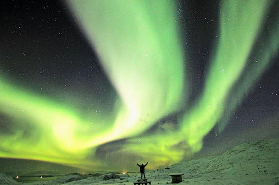 Bright aurora borealis over snowy landscape with person watching in Northern Norway