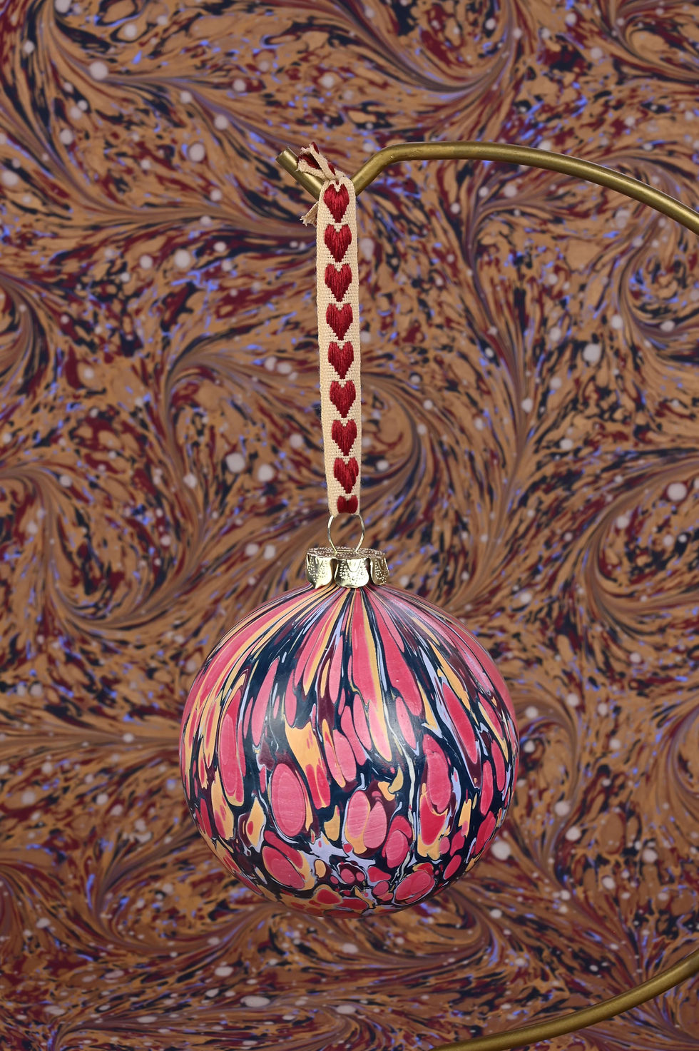 Thumbnail: Close up on a marbled bauble with an embroidered ribbon.