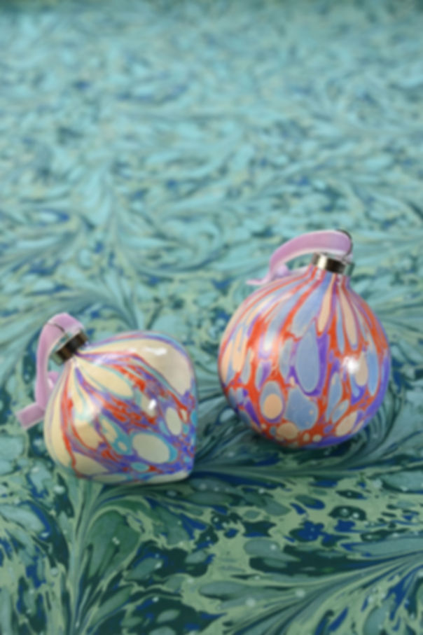 A set of two marbled ceramic baubles in light blue, purple and red, with velvet ribbon.