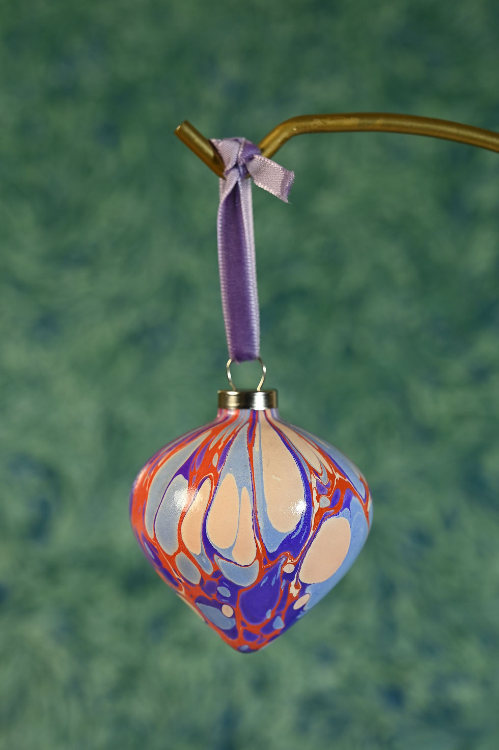Thumbnail: Close up on a marbled ceramic bauble hanging down, in tones of purple, red and light blue, with velvet ribbon.