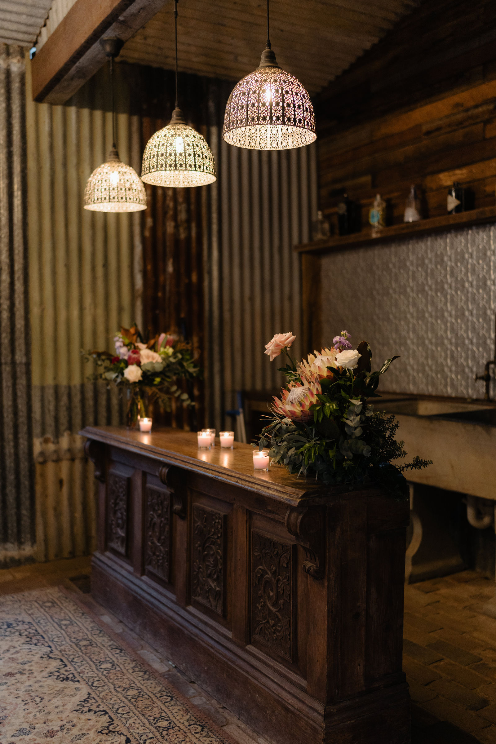 The carved vintage bar inside the Barn with pendant lights, candles and flowers