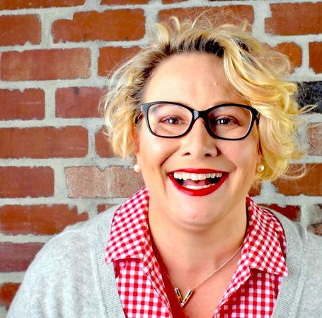 Happy, smiling blond woman with short curly bob, wearing eye glasses with black frames.
