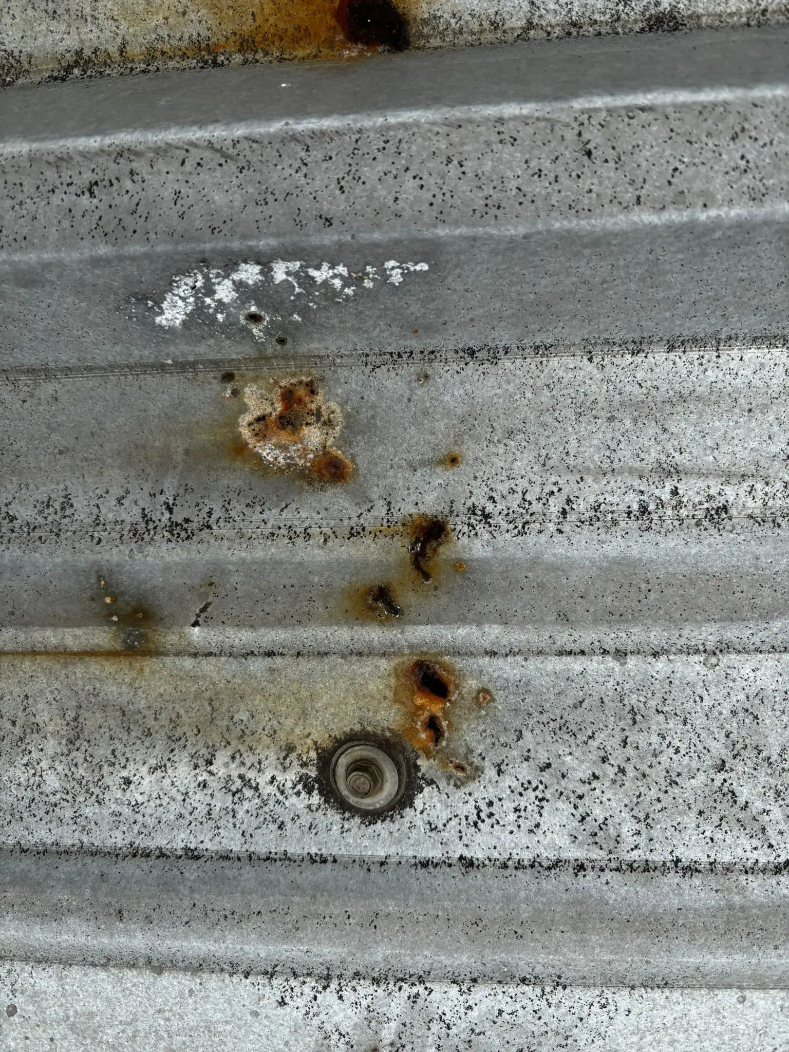 Schadensbild am Metalldach: Lokaler Korrosionsherd im Bereich einer defekten Verschraubung mit beginnender Unterrostung des Trapez-Blechdachs.