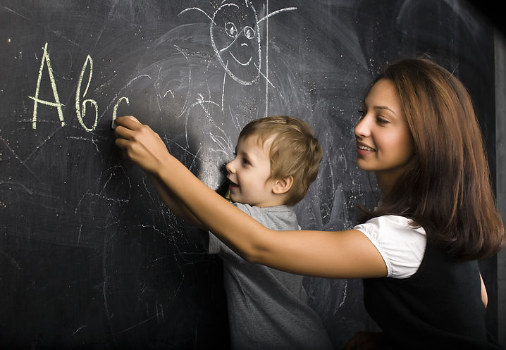 little cute boy with young teacher in classroom studying at blackboard smiling