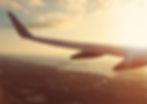 Airplane wing over a landscape with rivers at sunset, casting a warm, golden glow. Cloudy sky and vast horizon create a serene mood.
