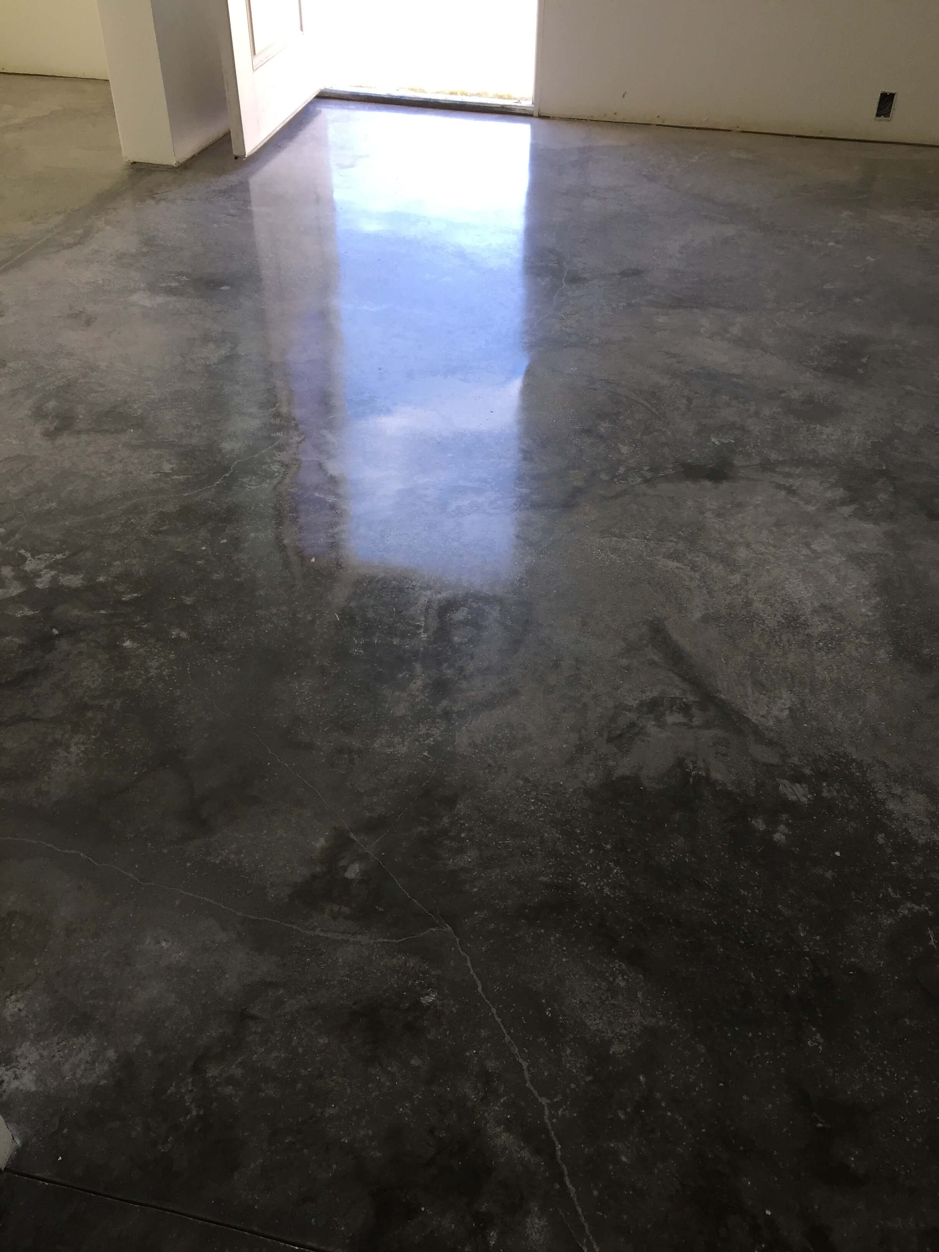 Dark stained polished concrete floor with a reflective surface and visible grid lines.