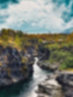 Río en cañón rocoso con árboles de otoño y cielo nublado