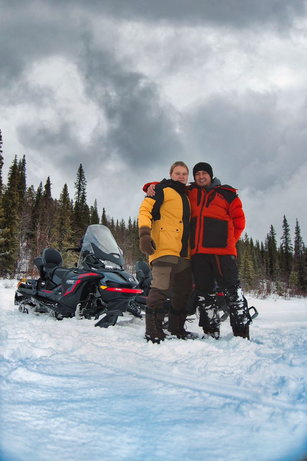 Dos hombres con chaquetas de invierno junto a una motonieve en la nieve