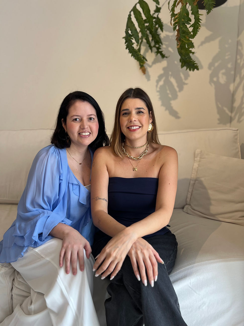 Duas consultoras da Mãe CLT sentadas lado a lado em um sofá, olhando para a câmera e sorrindo.