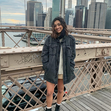 Copywriter Rhea Patil on the Brooklyn Bridge in front of an NYC skyline mid-day