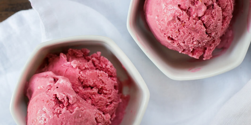 Two scoops of pink ice cream in white bowls on a soft white cloth background. The texture looks creamy and fresh.