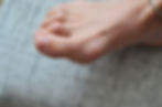 Close-up of a bare foot with hammertoes, wearing a silver anklet, resting on a gray textured surface. The background is softly blurred.