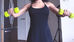 Woman in black dress exercises with lime green dumbbells in a room with a fridge and white door, creating a focused workout atmosphere.