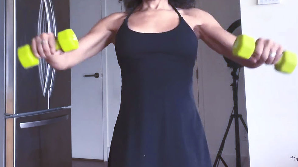 Woman in black dress exercises with lime green dumbbells in a room with a fridge and white door, creating a focused workout atmosphere.