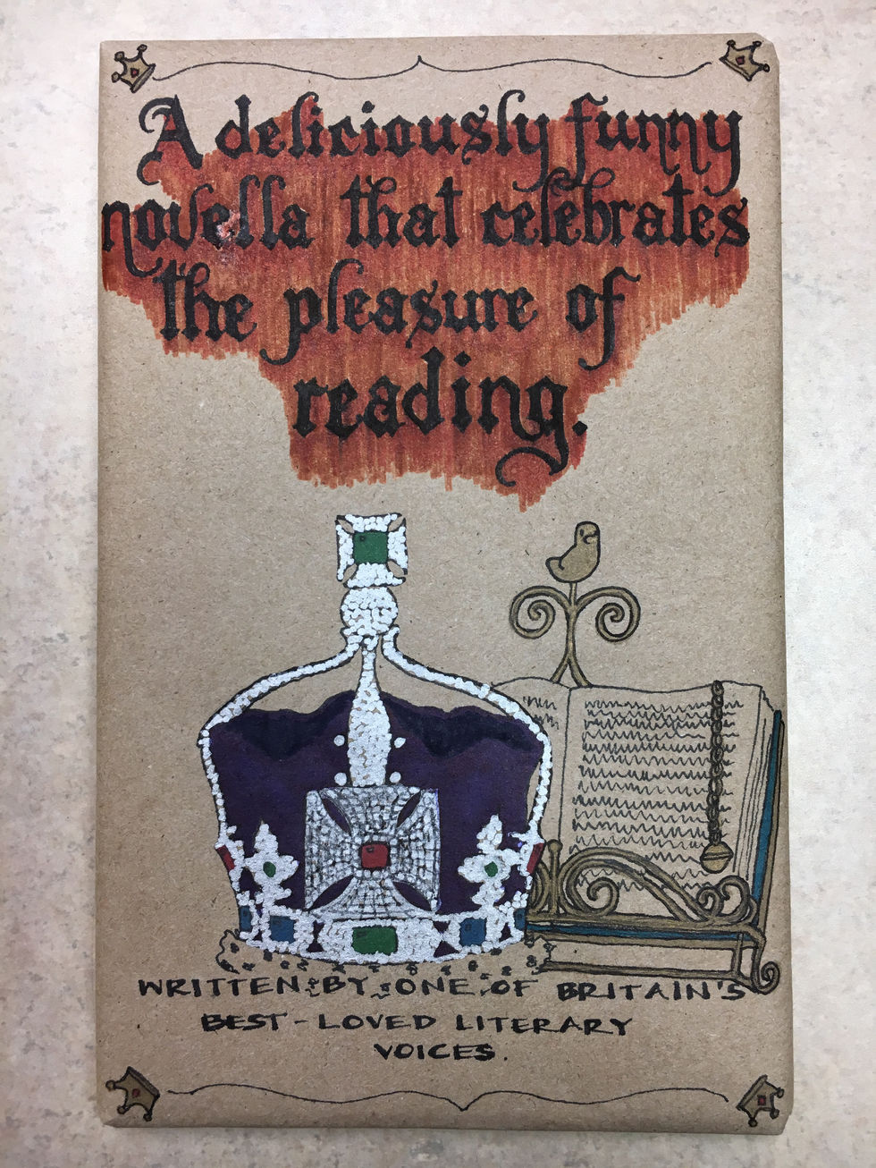 The Queen of England's crown, with a book in a fancy metallic holder behind it.