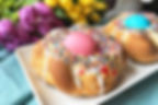 Italian Easter Bread sitting on a white plate on top of a blue napkin with purple and yellow flowers in the background. His Girl Sunday recipe tradition for Catholic Easter.